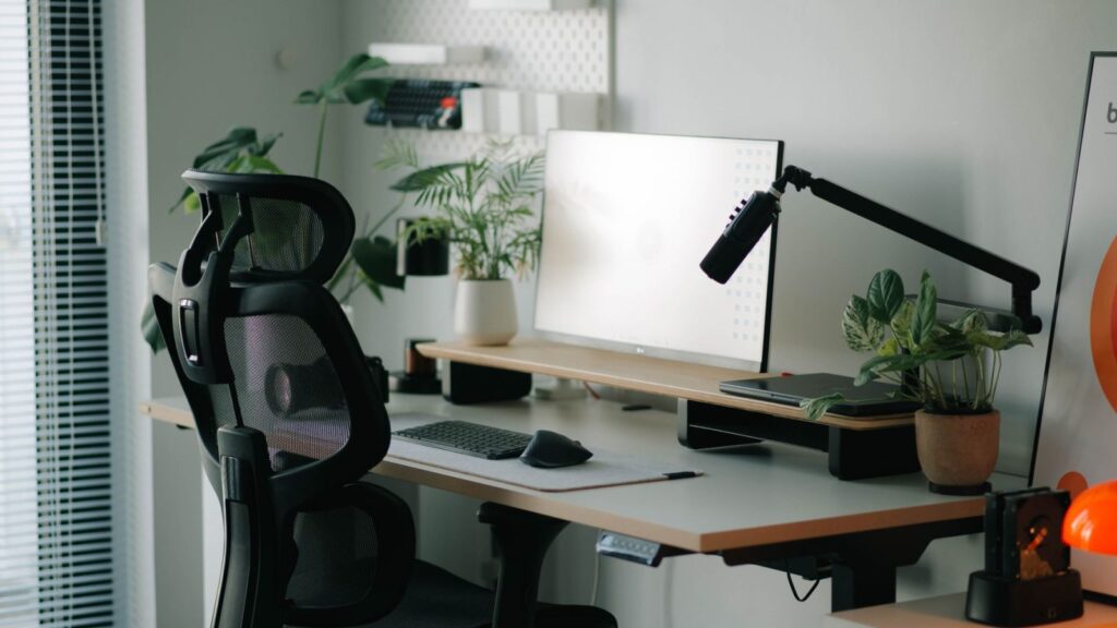 Žmogus sėdi ergonomiškoje kėdėje prie stalo, prie kompiuterio, su tinkama darbo poza