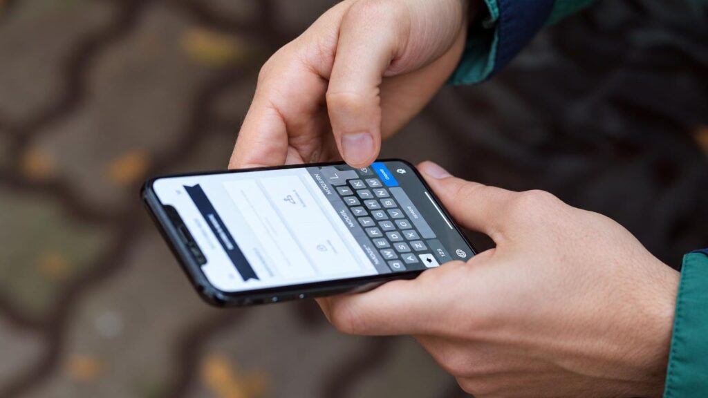 Rankos apžiūrinančios naudotą išmanųjį telefoną prie lango natūralioje šviesoje