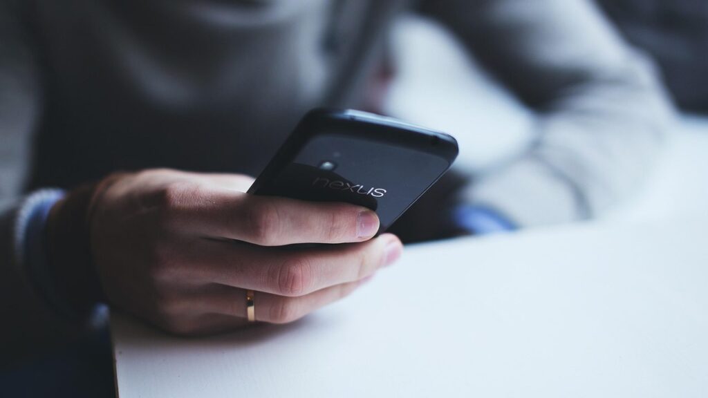 Išmanusis telefonas kelnių kišenėje žmogui einant gatve, fone – miesto aplinka