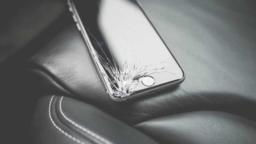 Išmaniojo telefono ekranas su smulkiais įbrėžimais, šalia raktai ir monetos