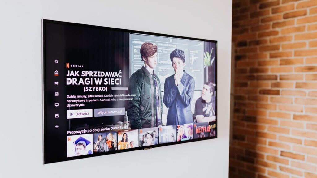 Žmogus svetainėje žiūri išmanųjį televizorių, transliuojantį laidą per internetą