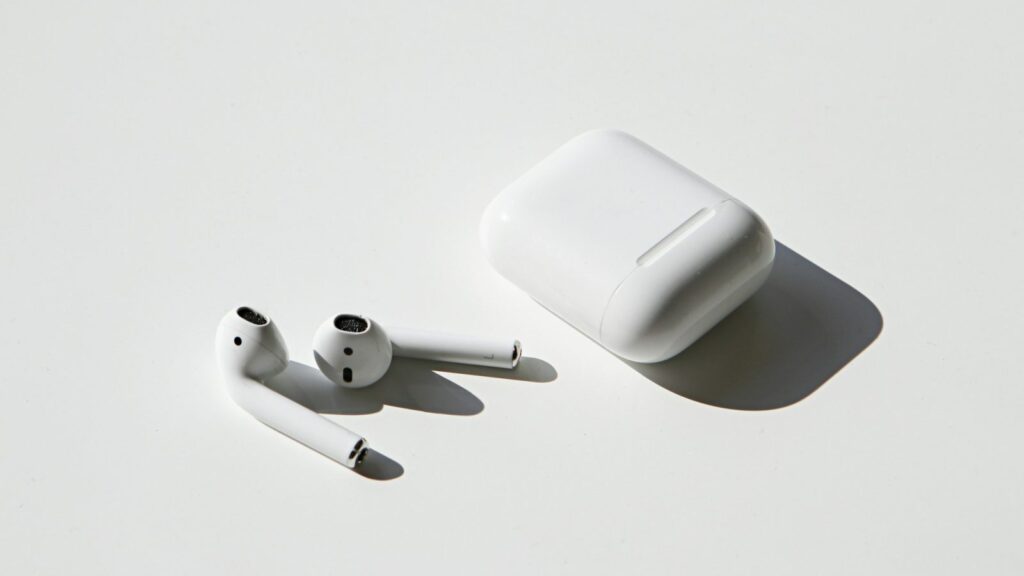Baltas AirPods ausinių dėklas su apsauginiu silikoniniu užvalkalu, laikomas rankoje