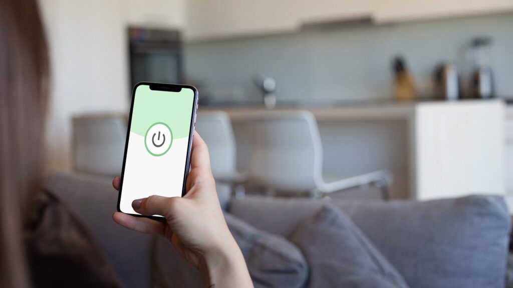 Žmogus naudojasi išmaniuoju telefonu prie lango, ekranas nukreiptas tik į save
