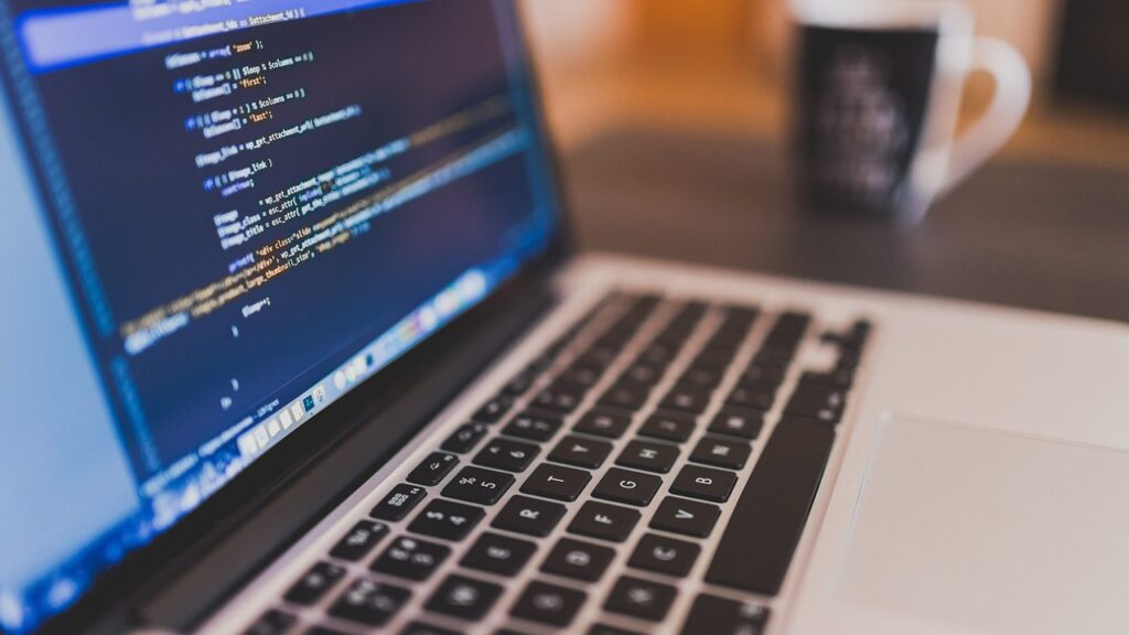 Programuotojas dirba prie nešiojamojo kompiuterio su kodu modernioje biuro aplinkoje