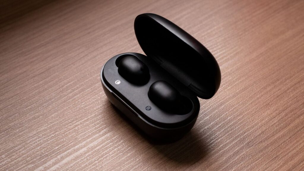 Belaidės ausinės šalia įkrovimo dėklo ant stalo – Bluetooth versijų palyginimas