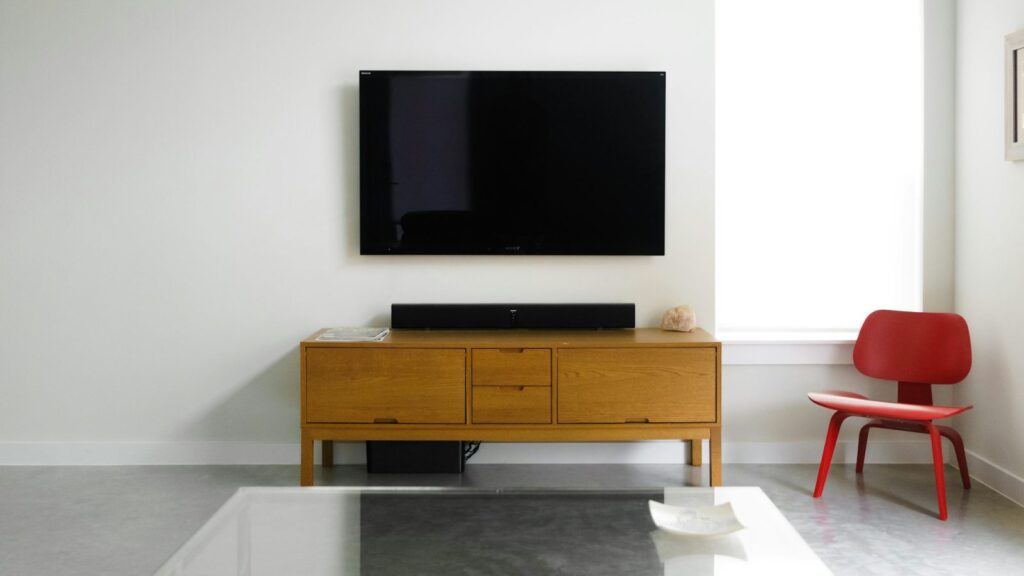 Juodas soundbar po plokščiu televizoriumi modernioje svetainėje