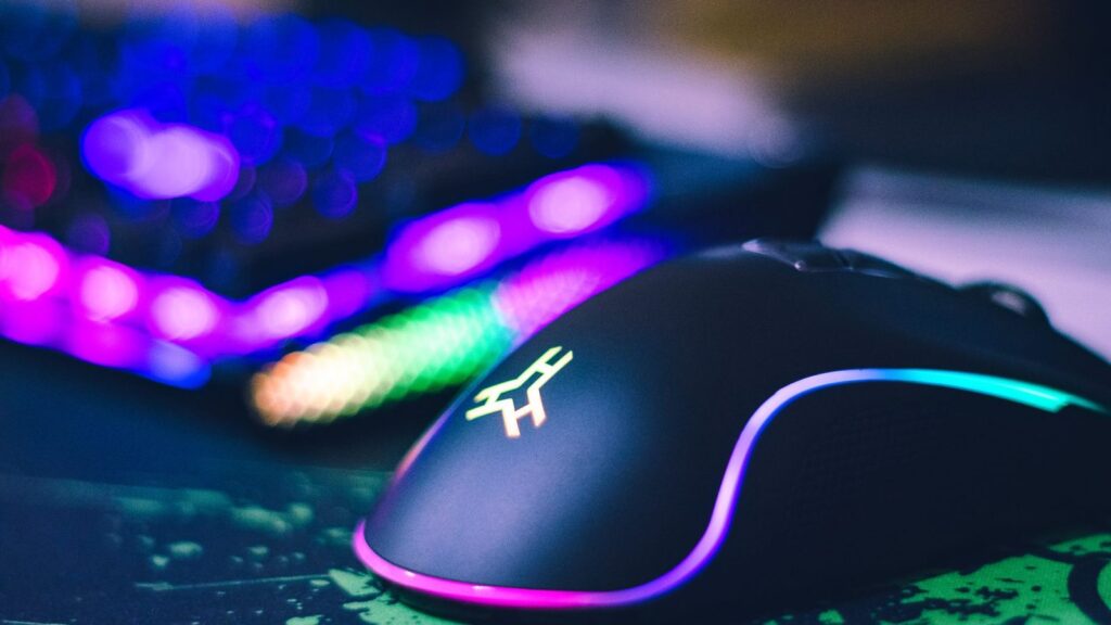 Juoda žaidimų pelė su šviečiančiu RGB apšvietimu ant žaidimų kilimėlio