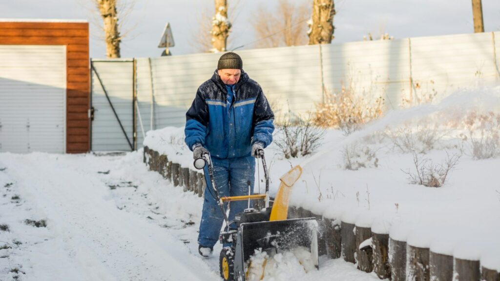 Elektrinis sniego valytuvas su laidu valo takelį prie namo po naujai prisnigusio sniego.