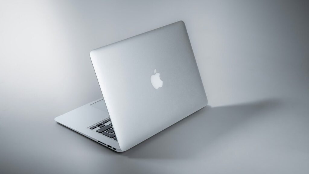 Sidabrinis MacBook nešiojamas kompiuteris ant stalo su tamsesniu ekranu, simbolizuojantis baterijos taupymą