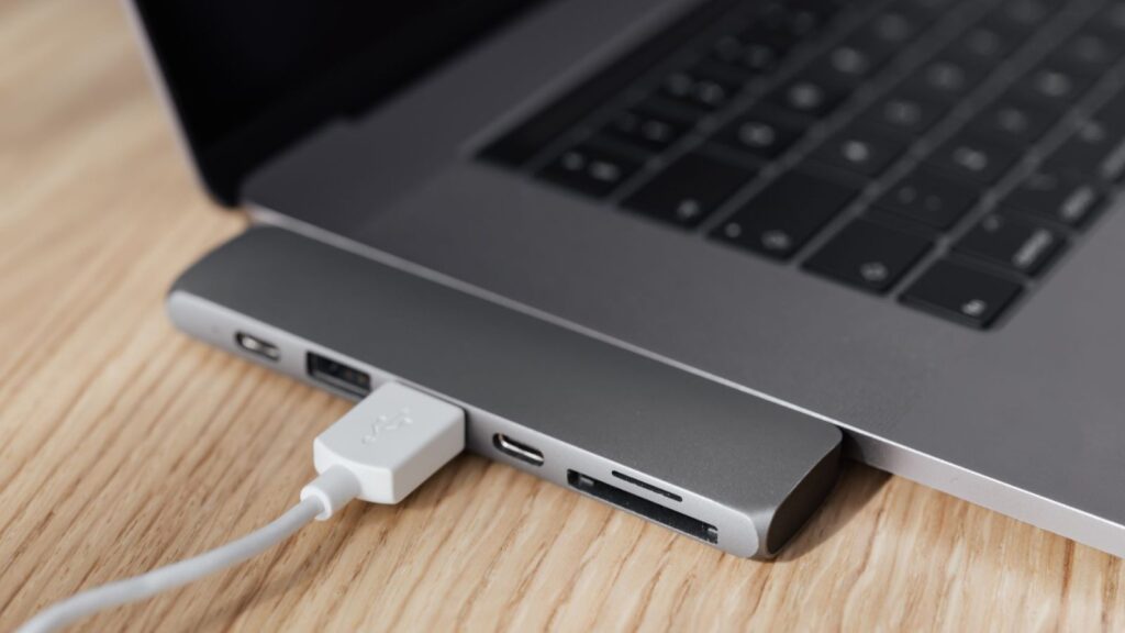 Maitinimo šaltinį turintis USB šakotuvas su prijungtais įrenginiais ant darbo stalo prie nešiojamojo kompiuterio