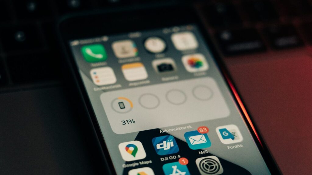 Rankos laiko iPhone telefoną, šalia įkrovimo laidas – tema apie baterijos būklės patikrinimą