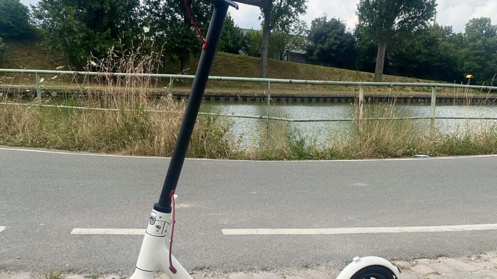 Paauglys su šalmu važiuoja elektriniu paspirtuku miesto dviračių take
